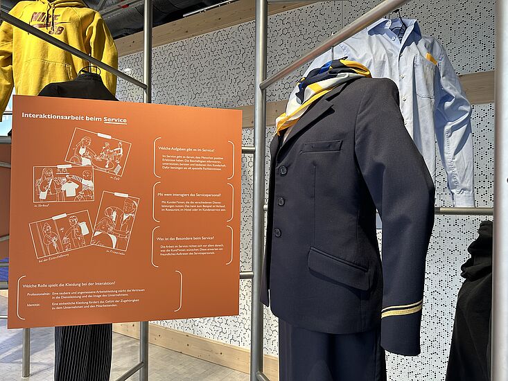 Kleiderstangen mit Dienstkleidung, etwa von einer Stewardess in der Ausstellung Dienstleistung